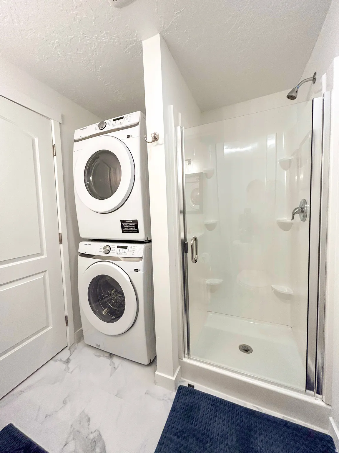 Contemporary bathroom featuring a glass-enclosed shower with integrated shelving and a stacked washer and dryer unit