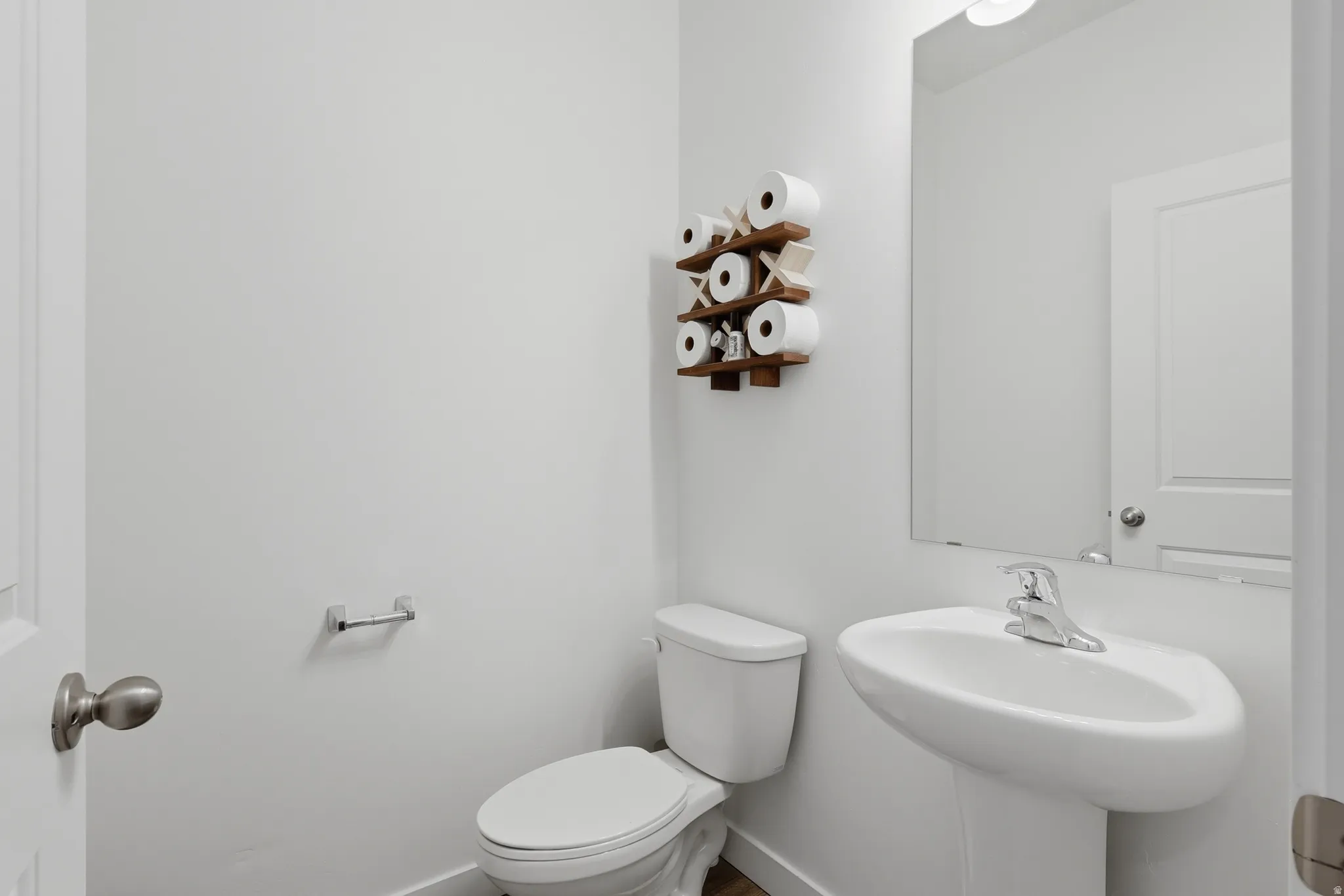Pedestal sink with chrome faucet, large wall-mounted mirror, and white toilet
