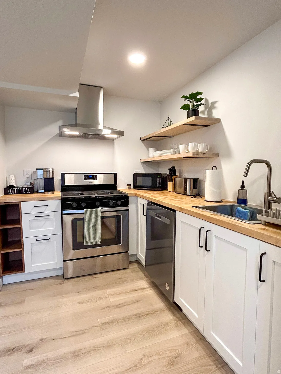 Contemporary kitchen featuring wood-finish flooring, white cabinetry with black hardware, and wood countertops