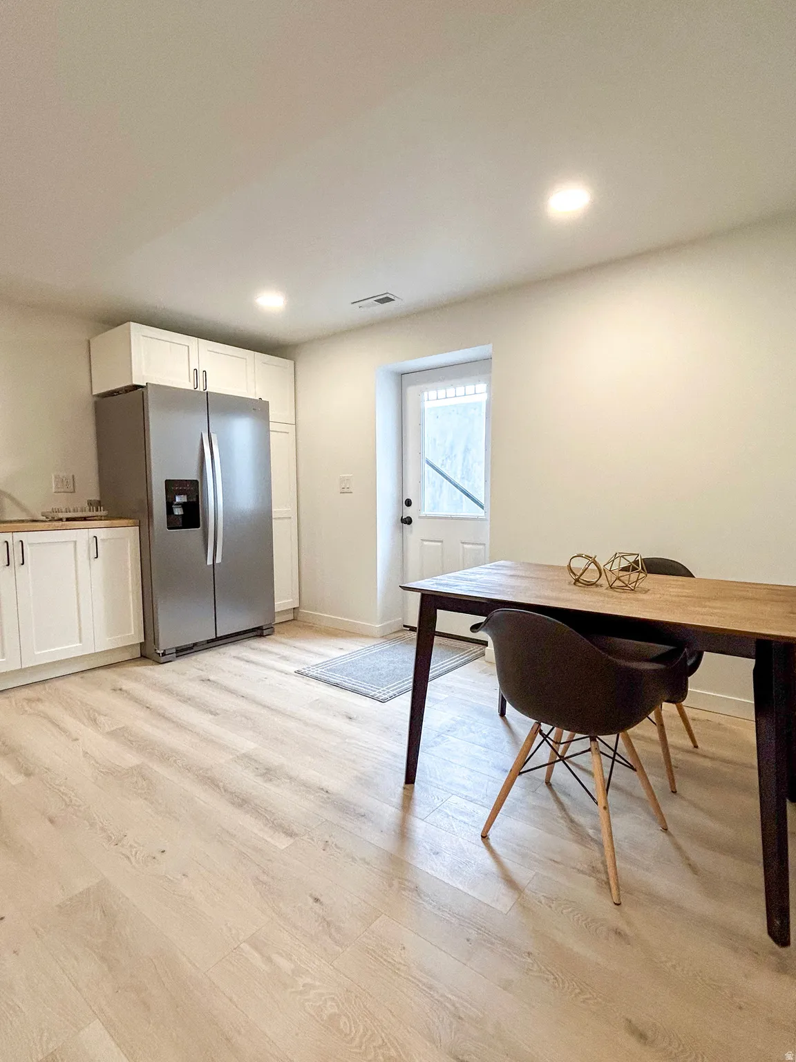 Open-concept kitchen and dining area featuring light wood-finish flooring, white cabinetry, recessed lighting, and a stainless steel refrigerator