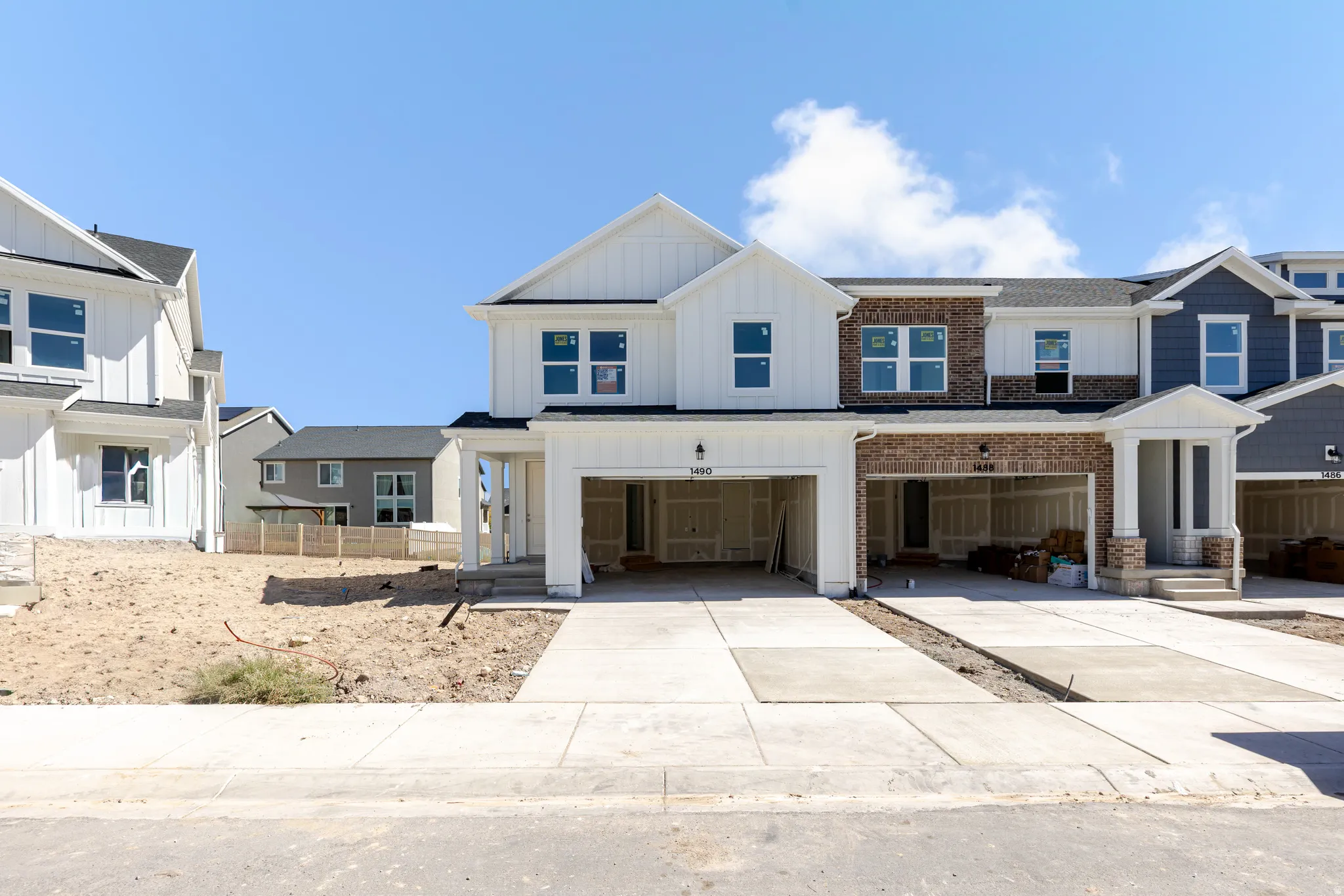 Modern townhome exterior featuring white board and batten siding, brick accents, and a two-car garage