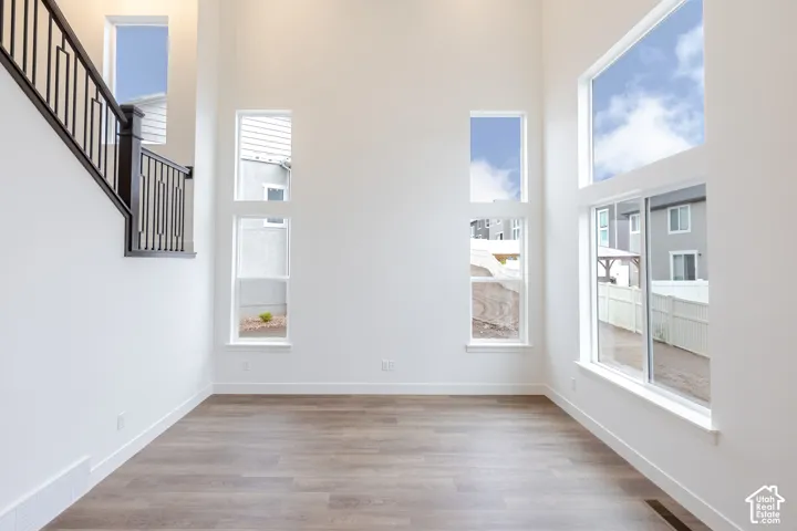 High ceilings featuring expansive multi-level windows, wood-finish flooring, and a staircase with a geometric metal railing