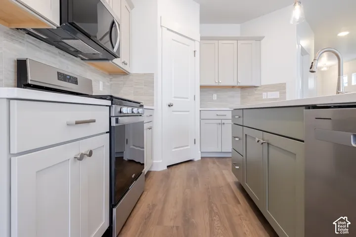 Kitchen featuring wood-finish flooring, stainless steel appliances, neutral shaker-style cabinetry, quartz countertops, and a tiled backsplash