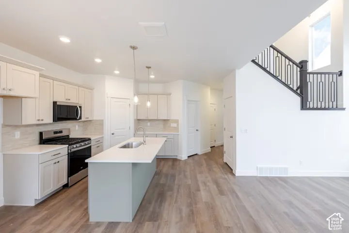 Kitchen featuring an island with a stone-finish countertop, stainless steel gas range, recessed lighting, wood-finish flooring, and a staircase with a black metal railing
