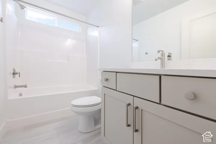 Bathroom featuring a vanity with light gray cabinetry, a neutral-toned stone countertop, an integrated sink with a polished metal faucet, a full-width wall mirror, and a tub-shower combination with a horizontal transom window