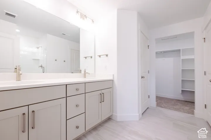 Dual-sink vanity with neutral cabinetry, expansive wall-to-wall mirror, solid-surface countertop, and walk-in closet featuring built-in shelving