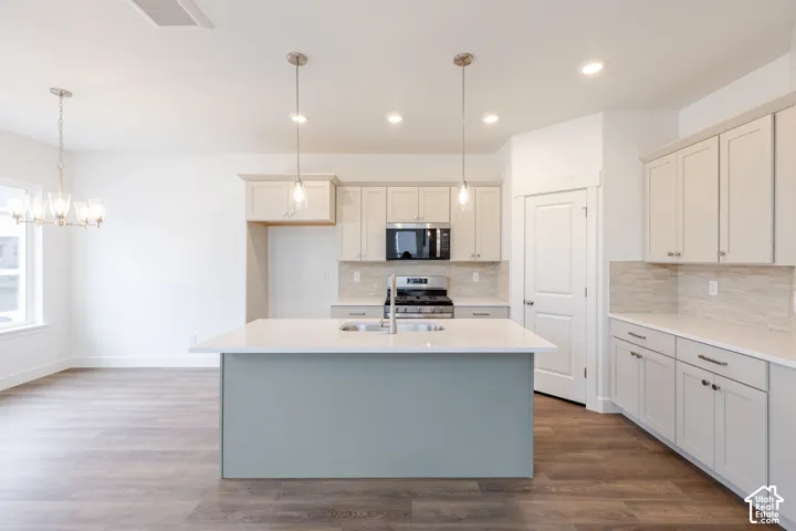 Kitchen featuring a central island with a solid surface countertop, wood-finish flooring, shaker-style cabinetry, recessed lighting, and glass pendant fixtures