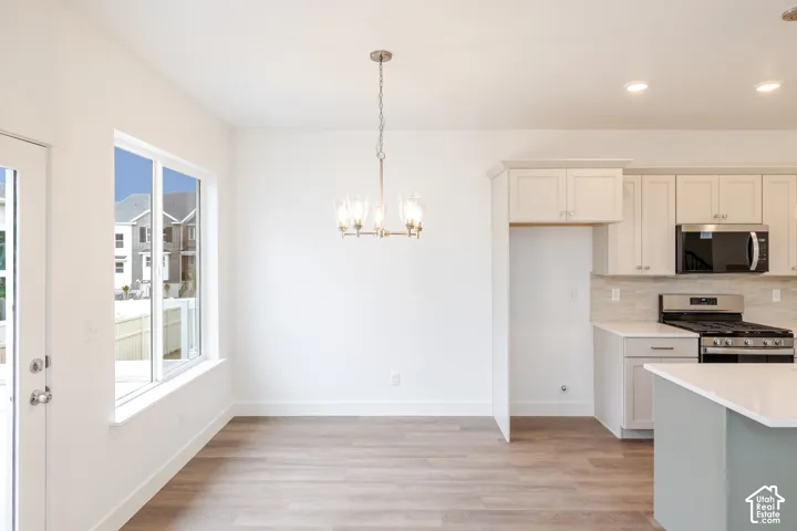 Kitchen featuring wood-finish flooring, white cabinetry, a neutral stone-texture backsplash, stainless steel appliances, and a central chandelier
