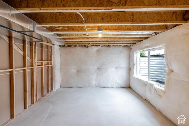 Unfinished room featuring exposed wooden wall framing, concrete flooring, exposed ceiling joists, insulated walls, and a recessed window with a corrugated metal well