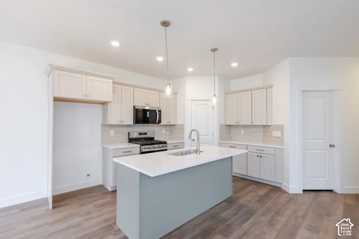 Kitchen featuring an island with a quartz countertop, neutral-toned cabinetry, stainless steel range with over-the-range microwave, tile backsplash, and wood-finish flooring