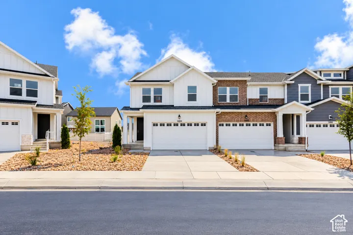Modern multi-level exterior featuring vertical board-and-batten siding, brick masonry, asphalt shingle roofing, and concrete driveways with attached multi-car garages