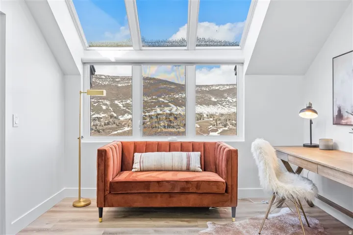 Bright room featuring a large skylight system, three expansive windows, clean white walls, light wood-finish flooring, and a built-in desk