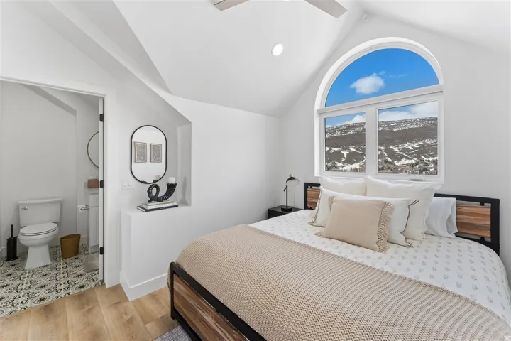 Arch-top window with transoms, vaulted ceiling, recessed lighting, wood-finish flooring, and an attached bathroom featuring patterned floor tiles