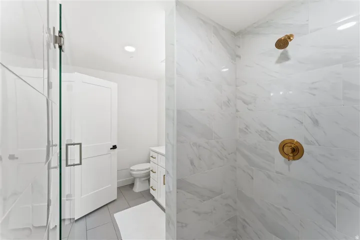 Walk-in shower featuring large format white tiled walls with subtle veining, a glass enclosure, and modern brass fixtures