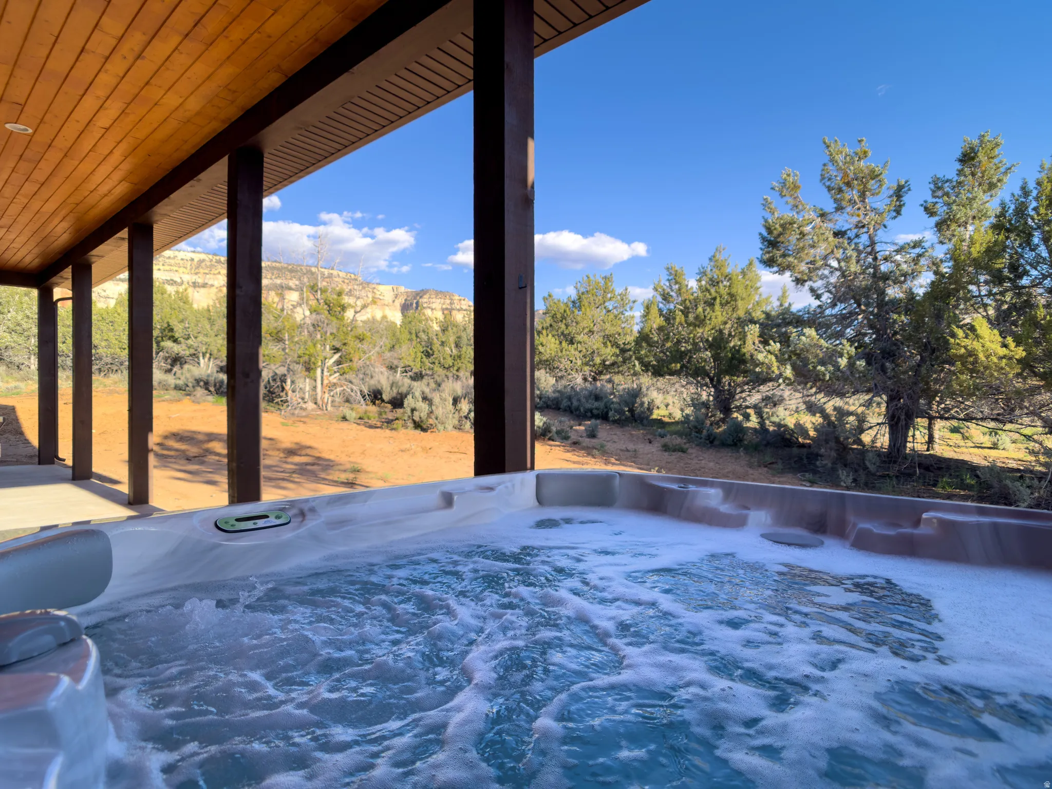 Outdoor spa tub with bubbling water under a covered patio featuring a wood-finish ceiling