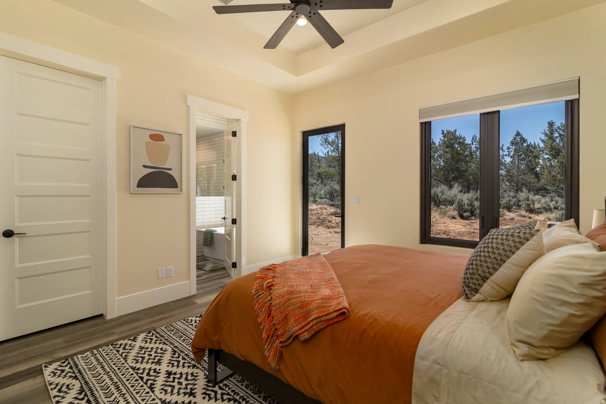 Primary bedroom featuring a tray ceiling with a ceiling fan, a large window with a desert landscape, a glass-paned door opening to the outdoors, and a five-panel interior door