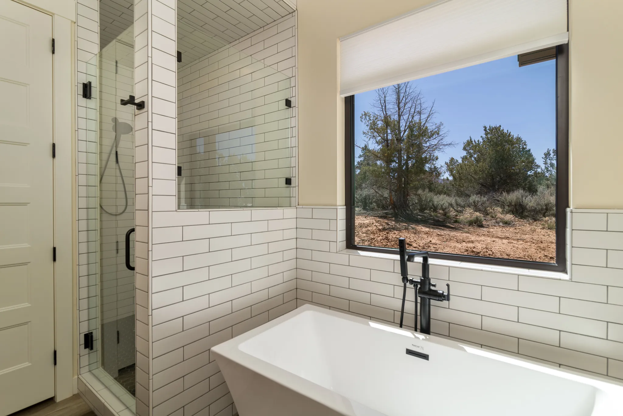 Modern primary bathroom featuring a freestanding tub with black floor-mounted faucet, a glass-enclosed shower, and subway tile walls