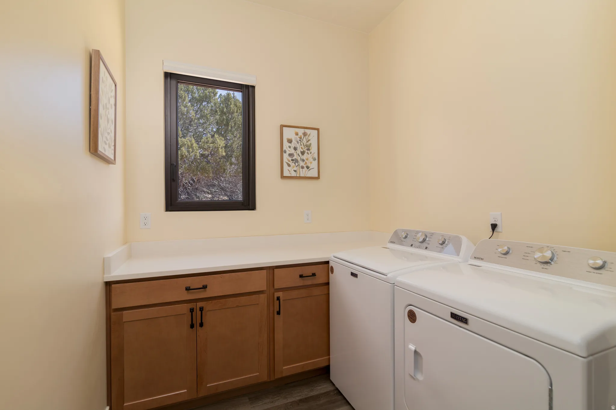 Laundry area featuring wood-finish cabinetry, light countertops, wood-finish flooring, and a single window
