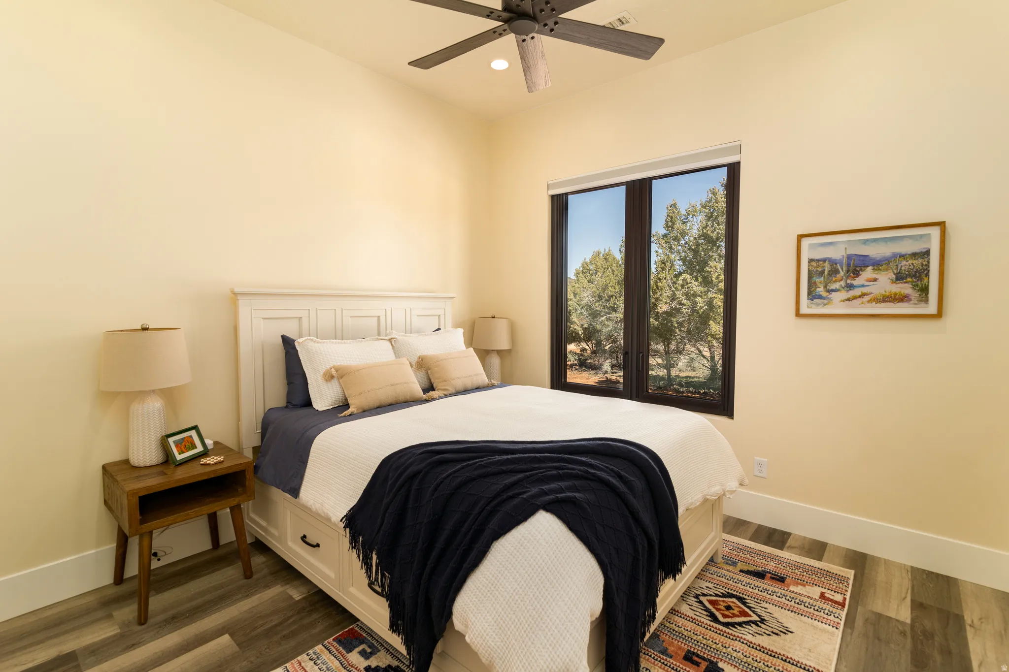 Spacious bedroom 2 featuring high ceilings, wood-finish flooring, and a large window with exterior tree scenery