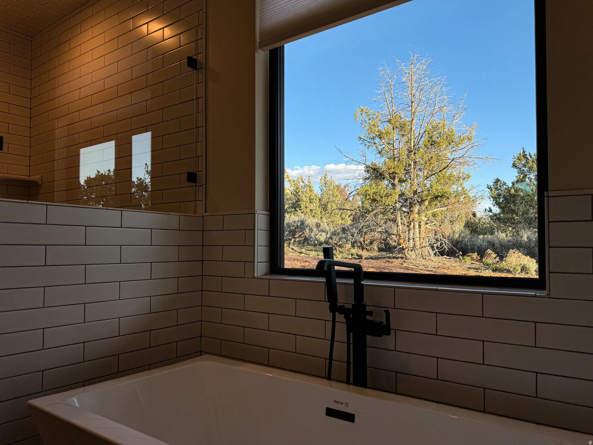 Primary bathroom featuring a freestanding tub with a floor-mounted matte black faucet, subway tile wainscoting, and a large picture window with a natural landscape backdrop
