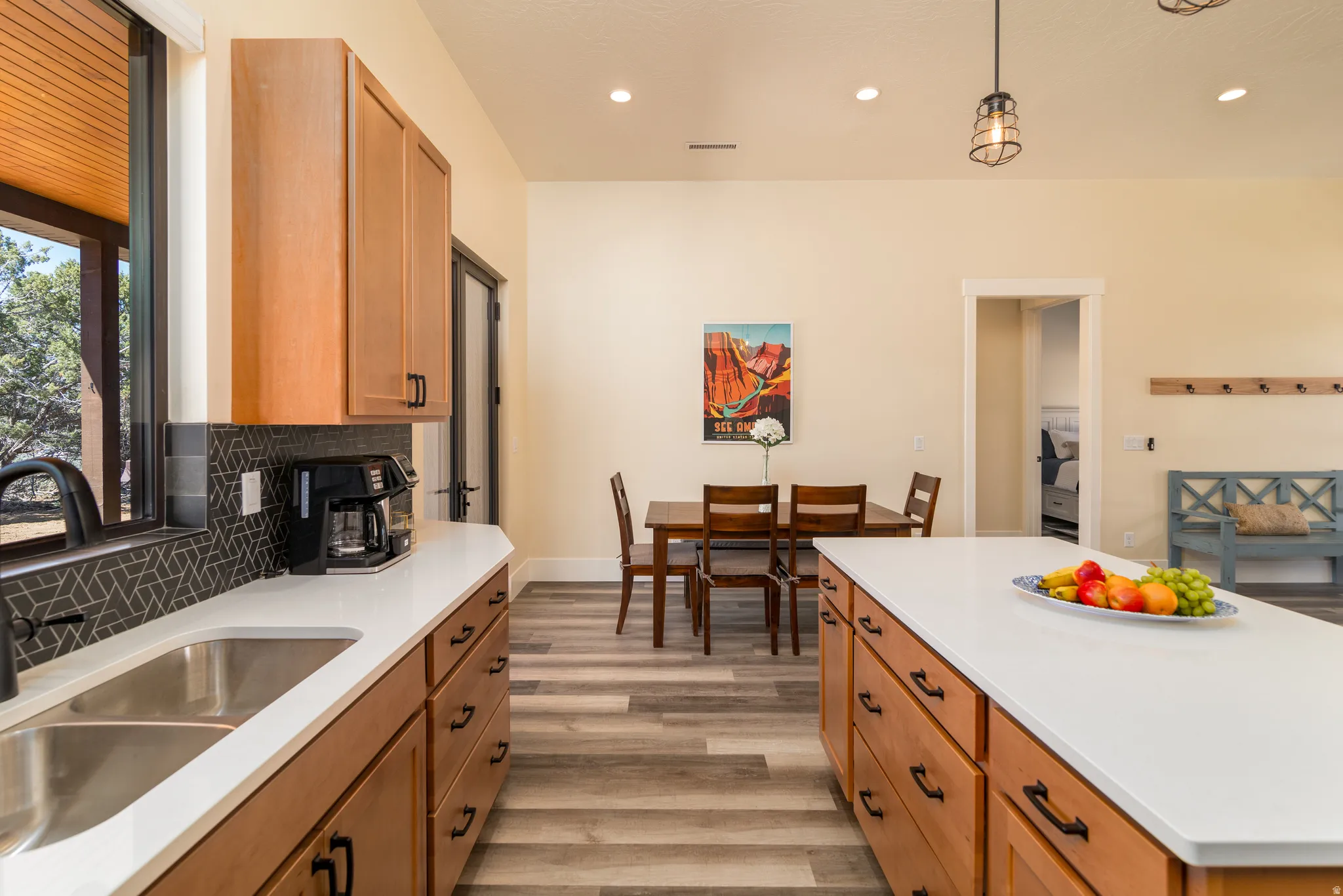 Open-concept kitchen and dining area featuring light wood-finish cabinetry, white countertops, a dual basin stainless steel sink, and wood-finish flooring