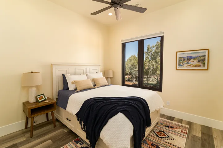 Spacious bedroom 2 featuring high ceilings, wood-finish flooring, and a large window with exterior tree scenery