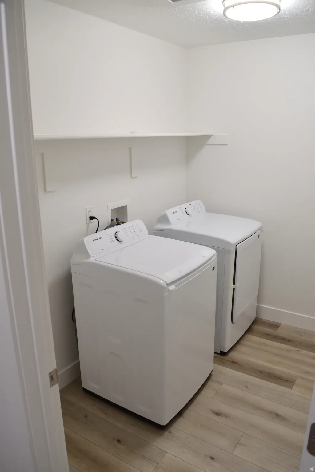 Dedicated laundry space with wood-finish flooring, white walls, and a built-in white shelf