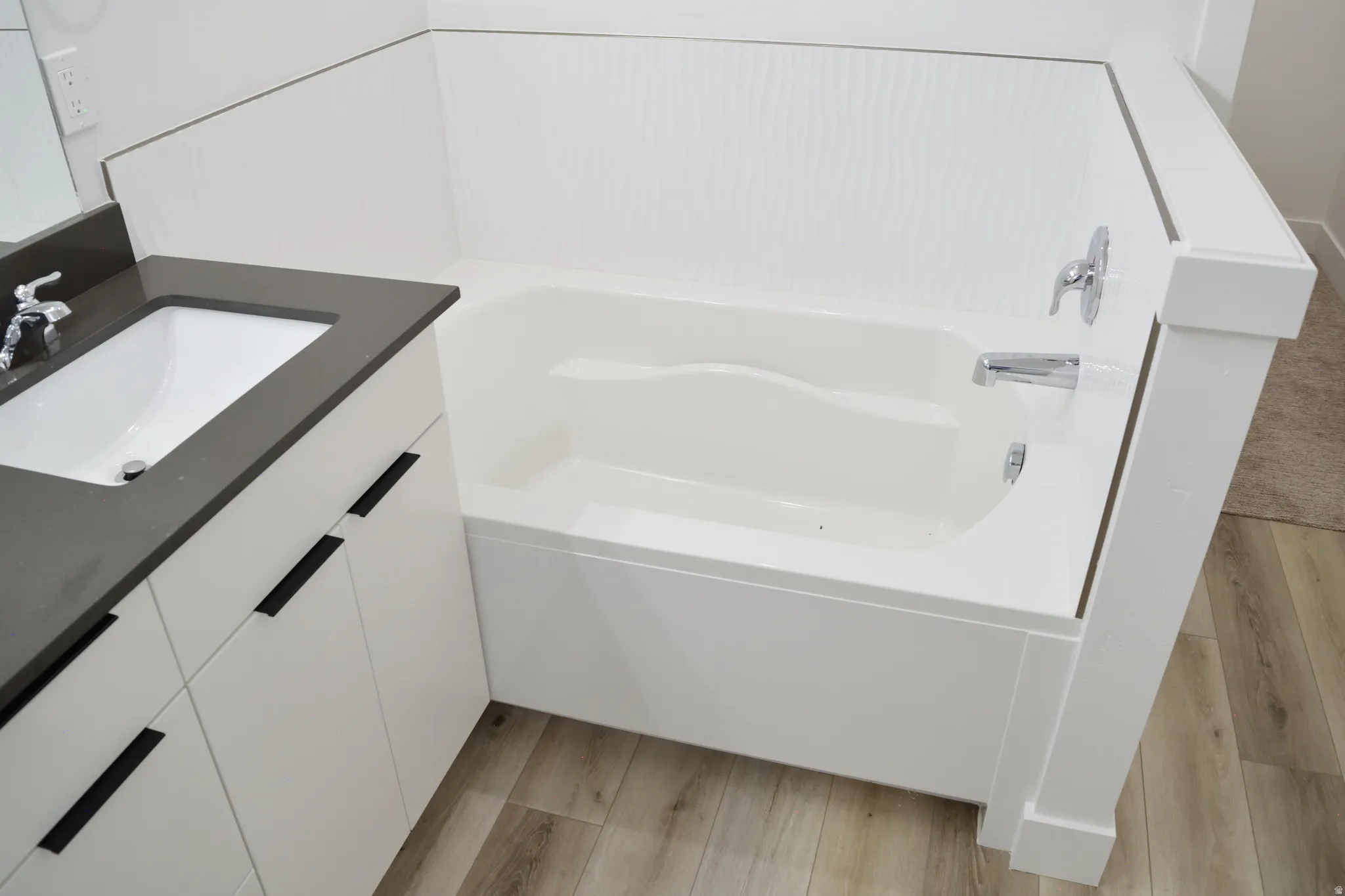 Modern bathroom featuring a white built-in bathtub with chrome fixtures, white vanity cabinetry, a dark countertop, and an integrated rectangular sink