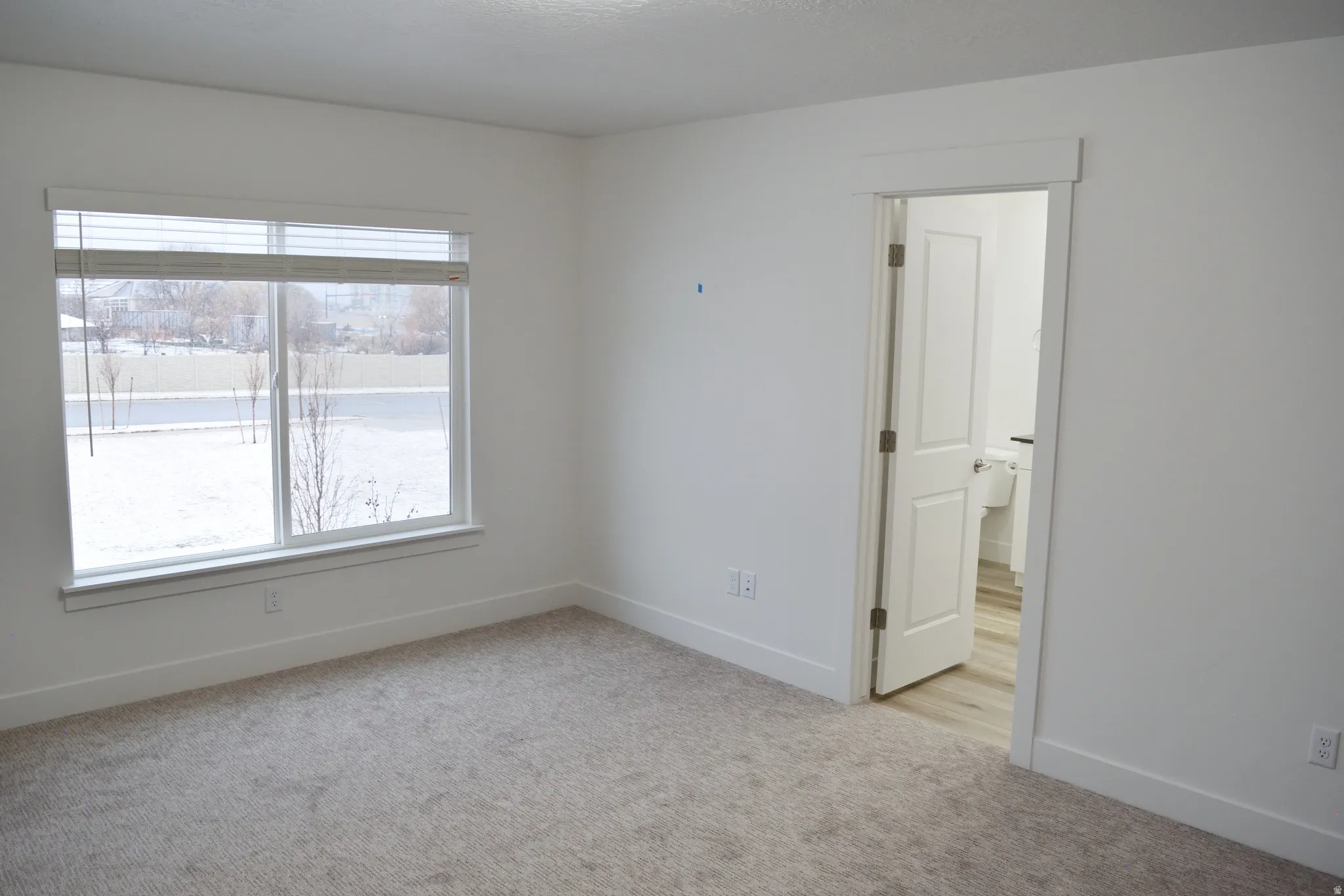 Bright interior space featuring a large window with white trim, neutral carpet, and white walls