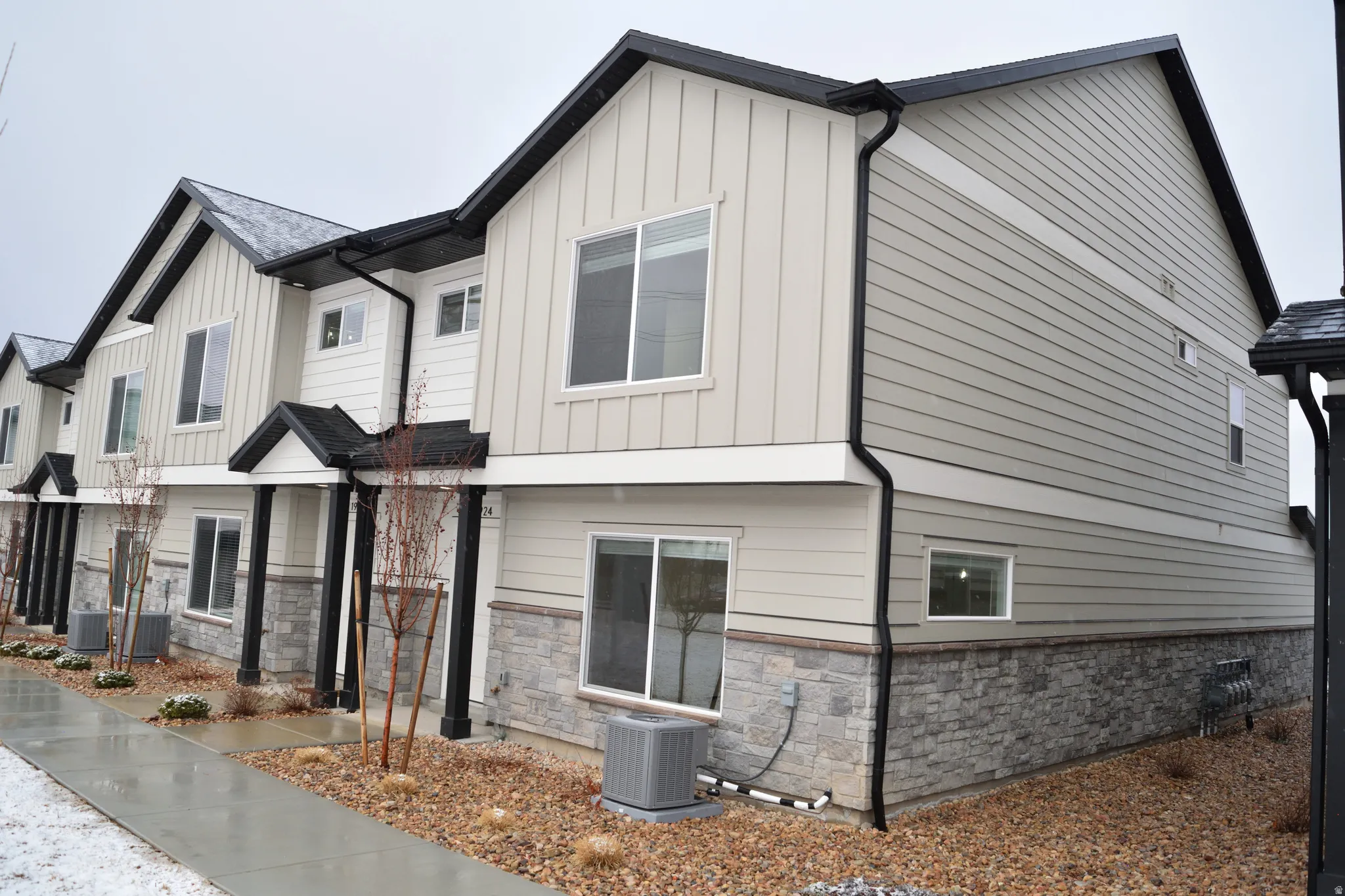 Modern townhome exterior featuring light-colored vertical and horizontal siding, dark roofing, stone veneer accents, and multiple windows