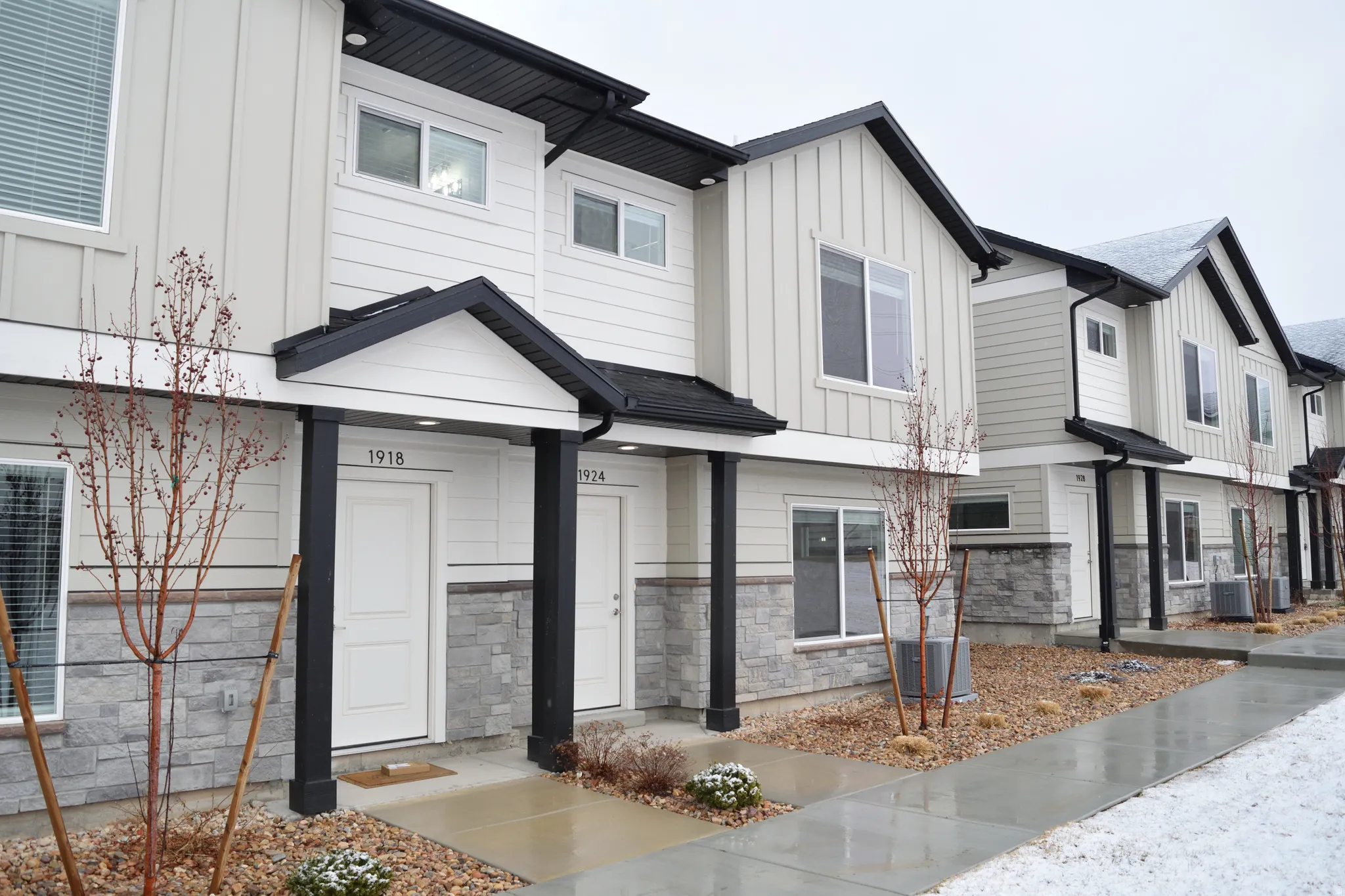 Townhome-style residences featuring light-colored siding, black trim, and a stone veneer foundation