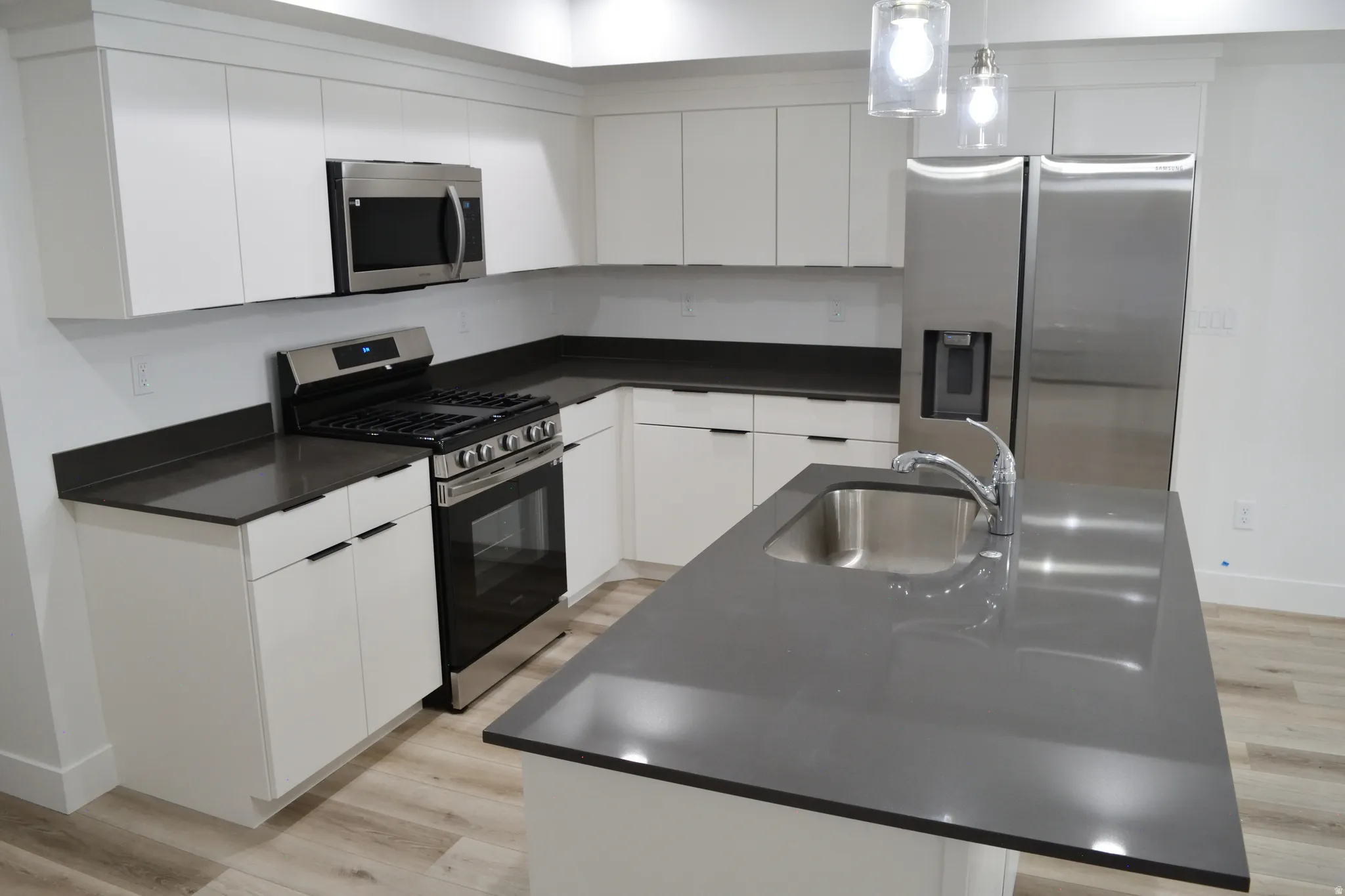 Modern kitchen featuring white cabinetry, dark countertops, stainless steel appliances, and wood-finish flooring
