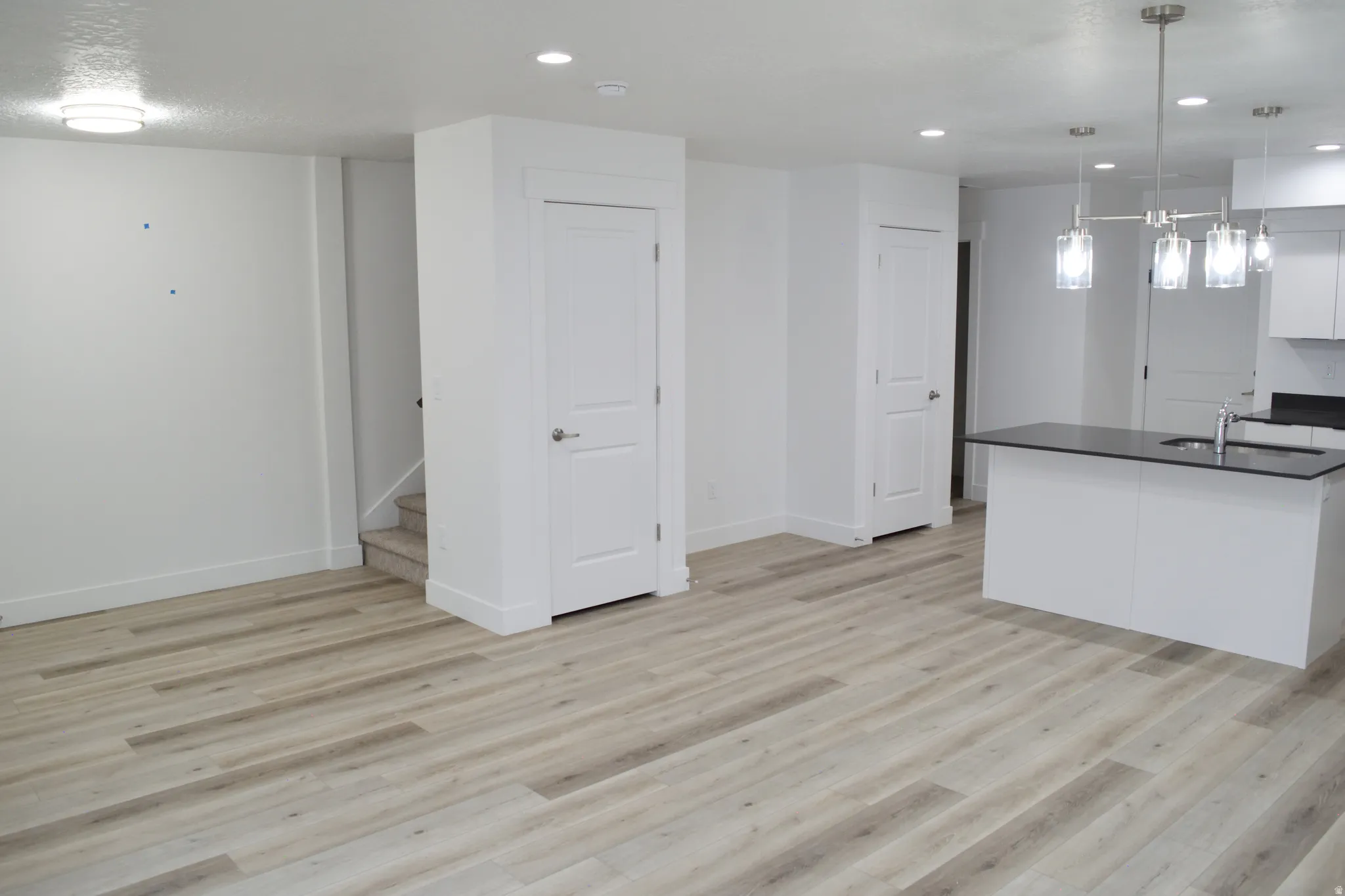 Open-concept living space featuring wood-finish flooring, recessed lighting, and a kitchen island with a dark countertop and sink