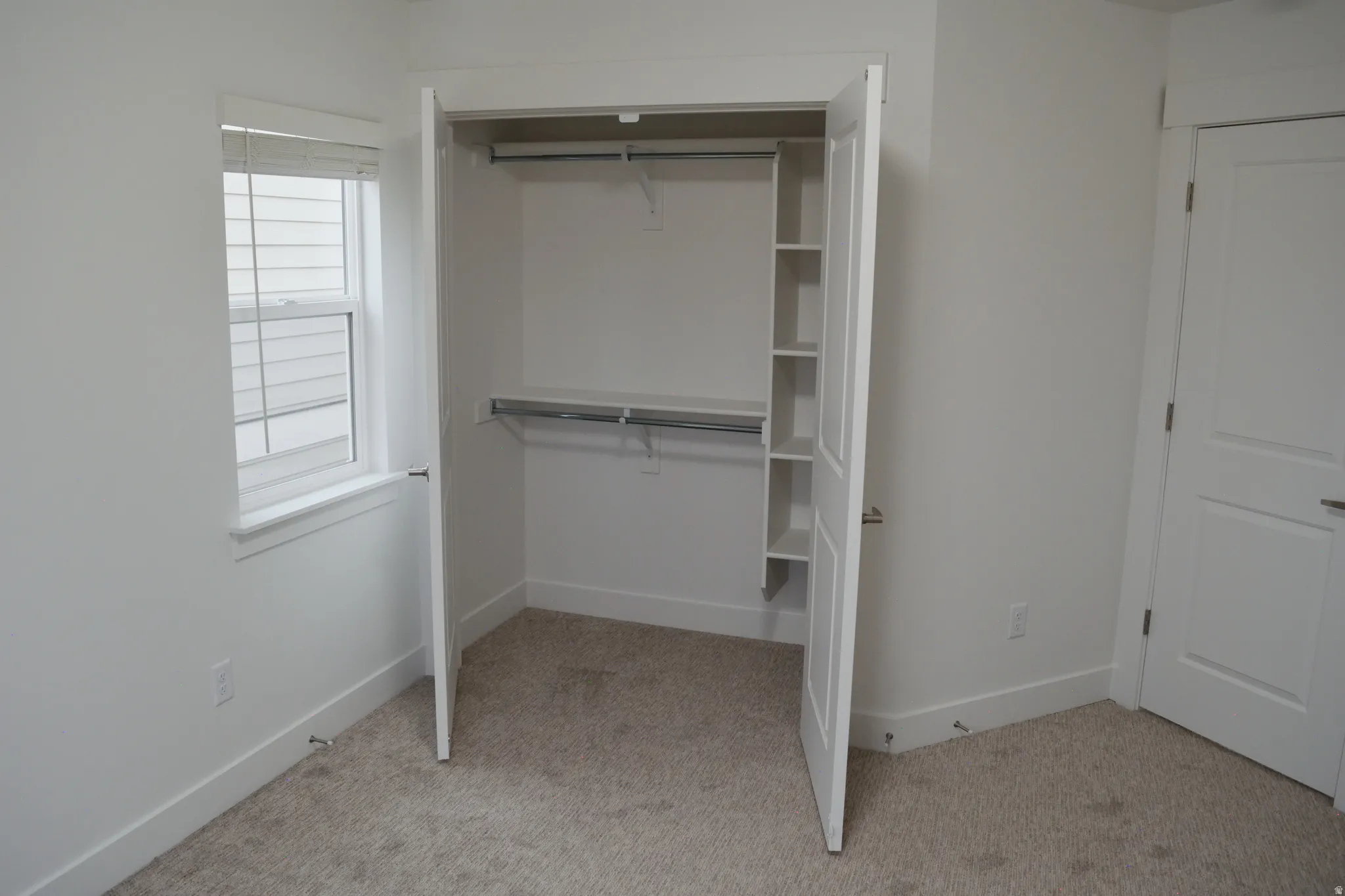 Custom closet system featuring built-in shelving and dual hanging rods, situated within a room with neutral-toned carpeting and white walls