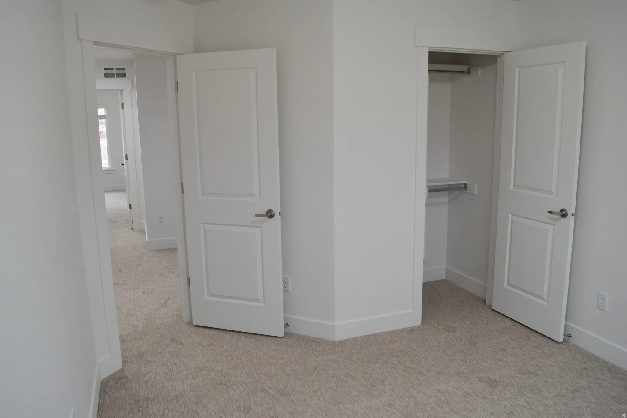Carpeted interior space featuring a double-panel interior door with brushed nickel hardware, a closet with shelving and hanging rod, light neutral wall paint, and white baseboards