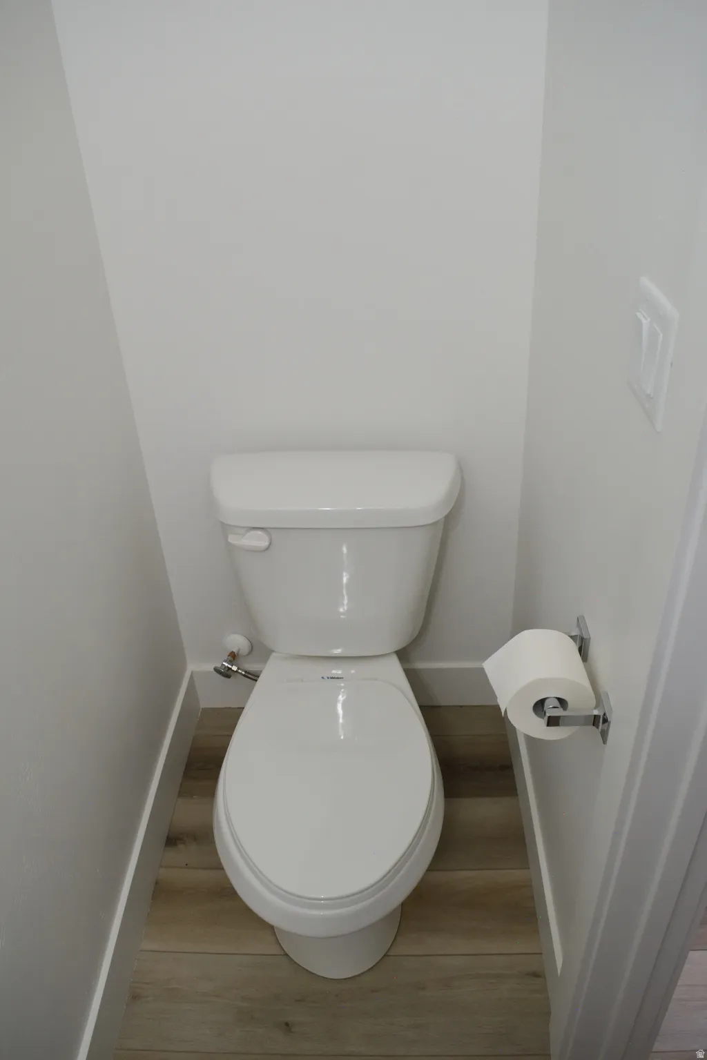 White ceramic commode with a tank and oval-shaped bowl, set against light-colored walls