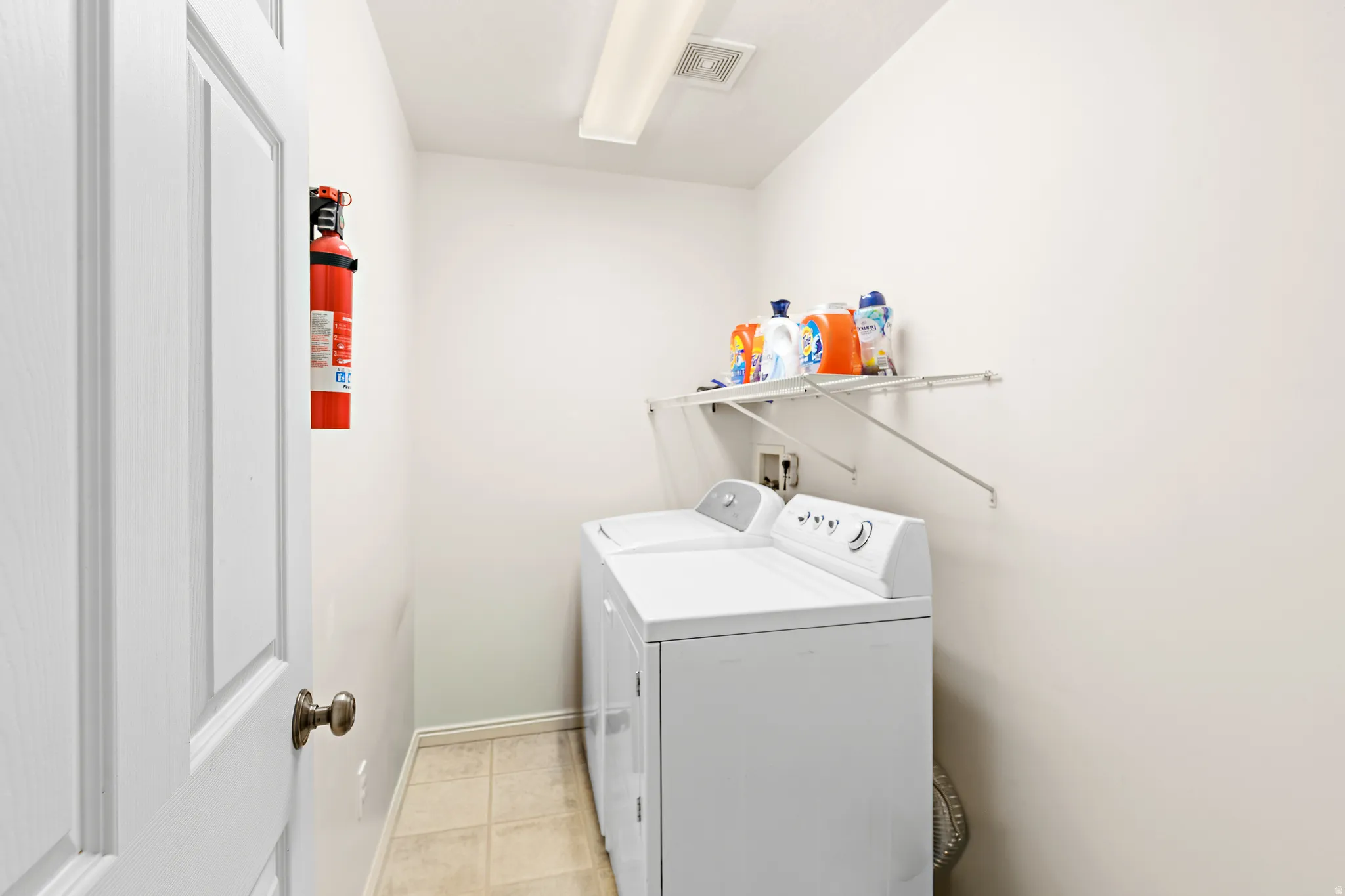 Dedicated laundry area featuring a washer and dryer set, neutral wall paint, and a wall-mounted wire shelving unit for storage