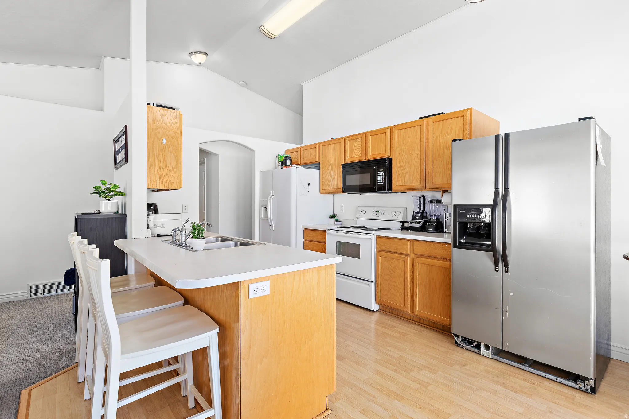 Kitchen featuring wood-finish flooring, light wood cabinetry, white countertops, and vaulted ceilings