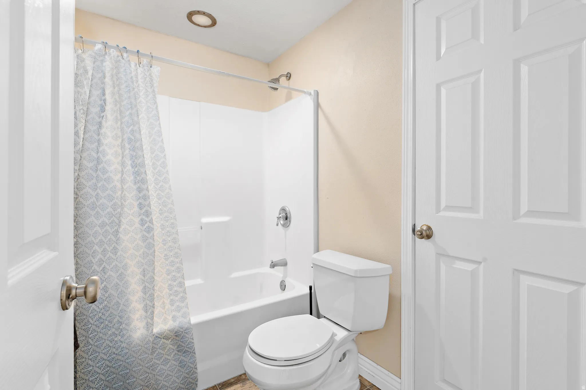 Full bathtub and shower combination with white surround, complemented by a contemporary toilet, neutral wall tones, and overhead recessed lighting