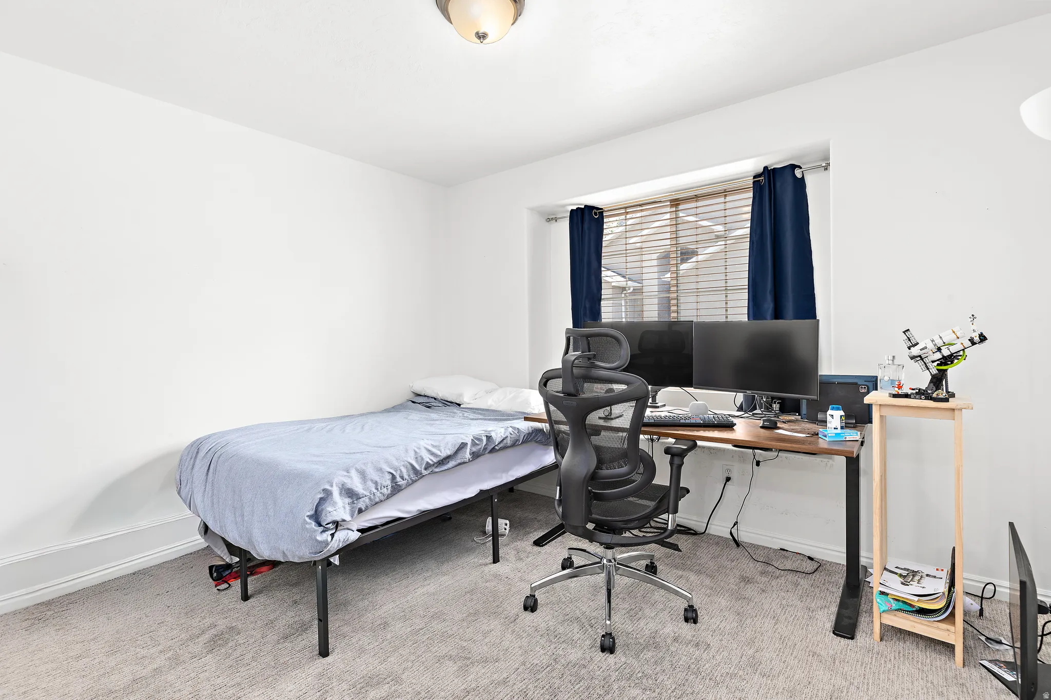 Bright room featuring white walls, a window with horizontal blinds and blue drapes, and a flush-mount ceiling light fixture