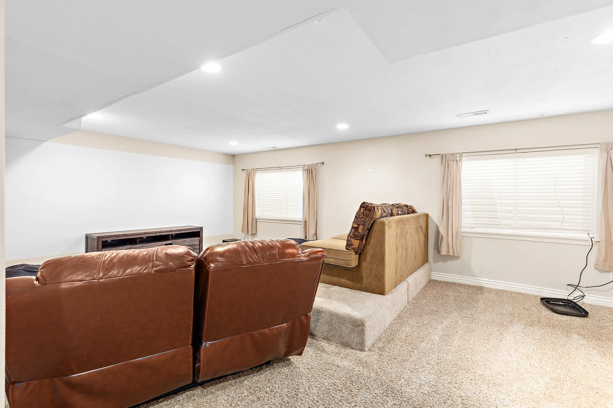Carpeted entertainment area featuring recessed lighting, a raised platform, and two windows with blinds