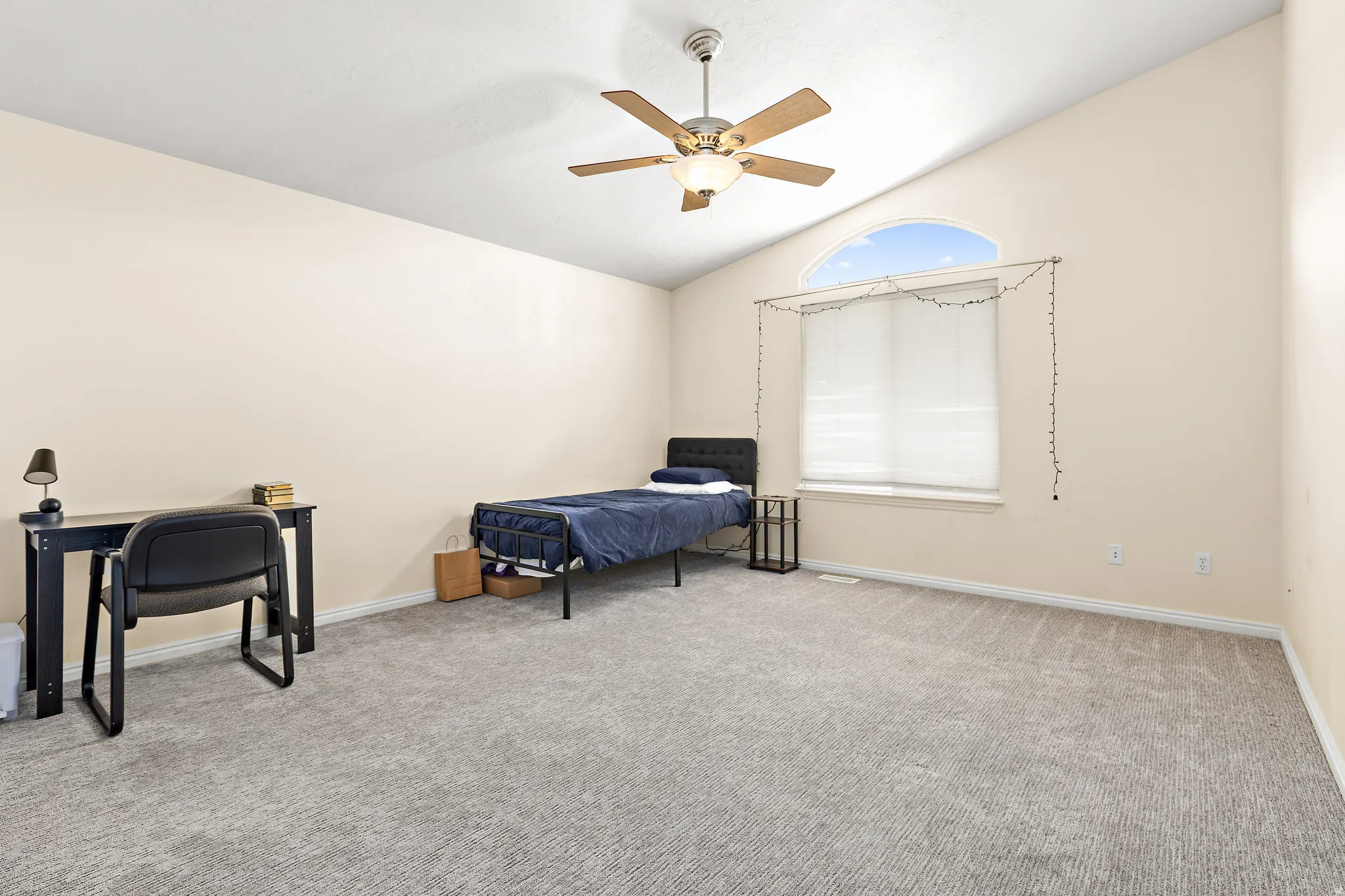 Expansive room featuring vaulted ceilings, a large arched window with white blinds, a ceiling fan with integrated lighting, neutral-toned walls, and grey patterned carpeting