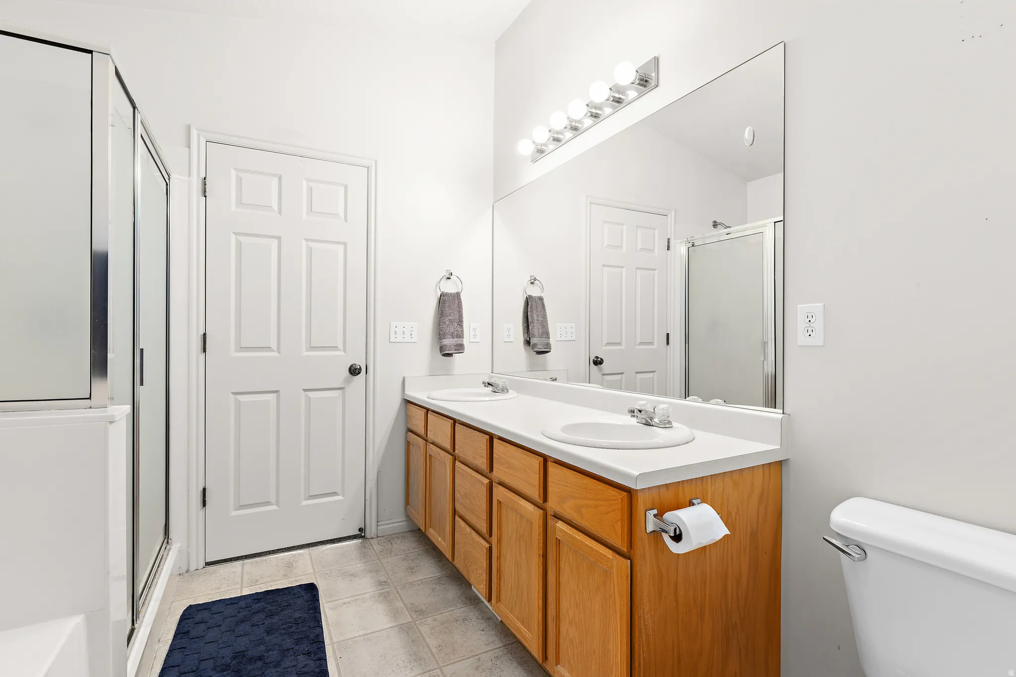 Bathroom featuring a dual vanity with light wood cabinetry, a built-in shower with clear glass enclosure, and neutral tile flooring