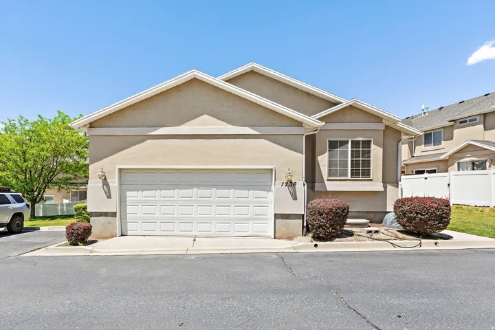 Stucco exterior featuring a two-car garage with panel detailing, decorative exterior lighting, and a prominent front window with grid patterns