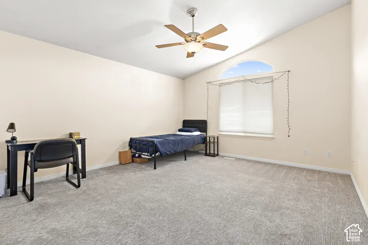 Expansive room featuring vaulted ceilings, a large arched window with white blinds, a ceiling fan with integrated lighting, neutral-toned walls, and grey patterned carpeting