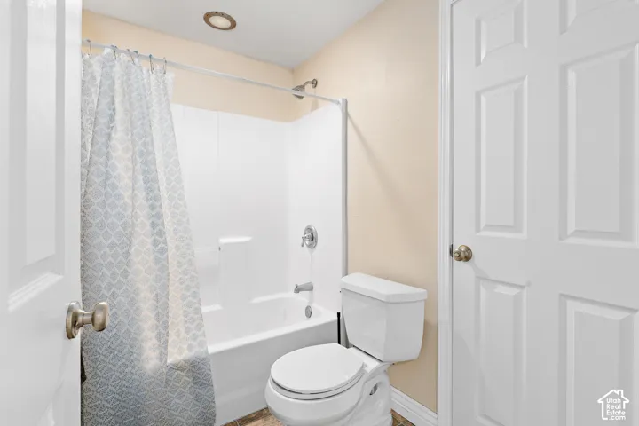 Full bathtub and shower combination with white surround, complemented by a contemporary toilet, neutral wall tones, and overhead recessed lighting