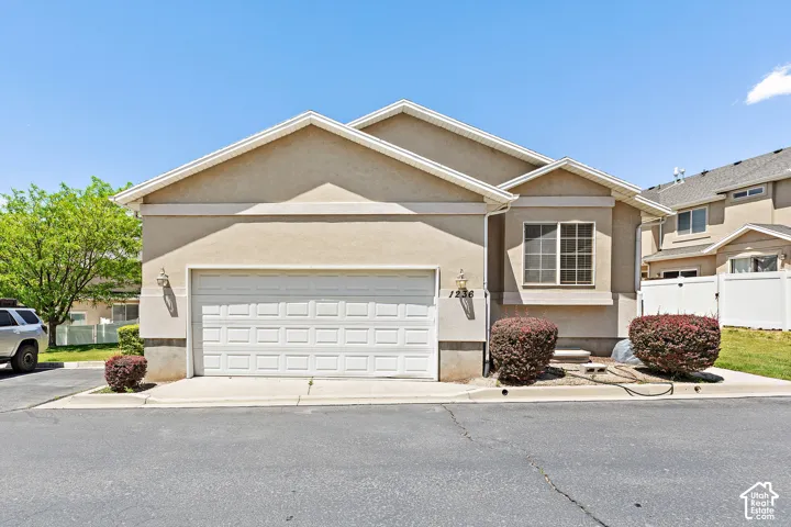 Stucco exterior featuring a two-car garage with panel detailing, decorative exterior lighting, and a prominent front window with grid patterns