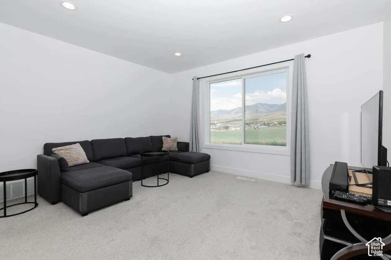 Spacious room featuring light gray carpeting, recessed ceiling lighting, a large window with white trim, and white baseboards right at the top of the stairs