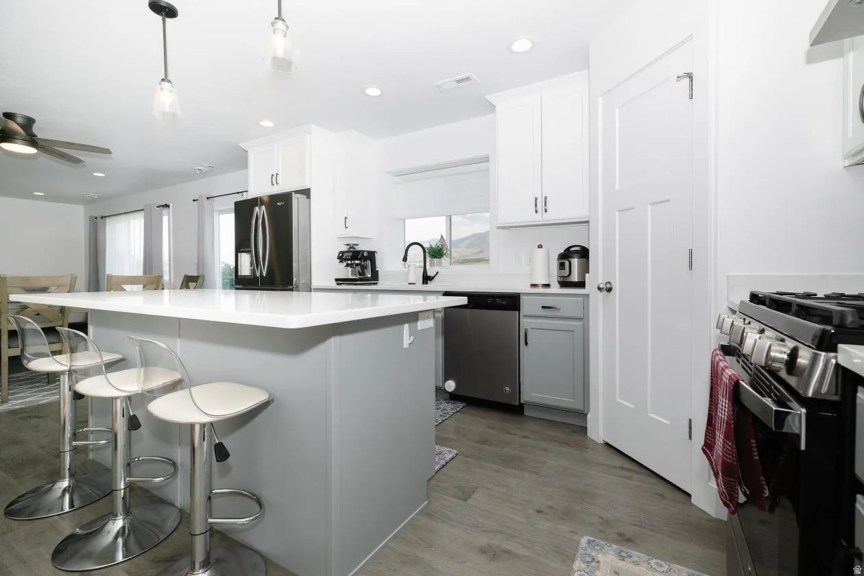 Contemporary kitchen featuring a large island with a light countertop, white upper cabinetry, and stainless steel appliances