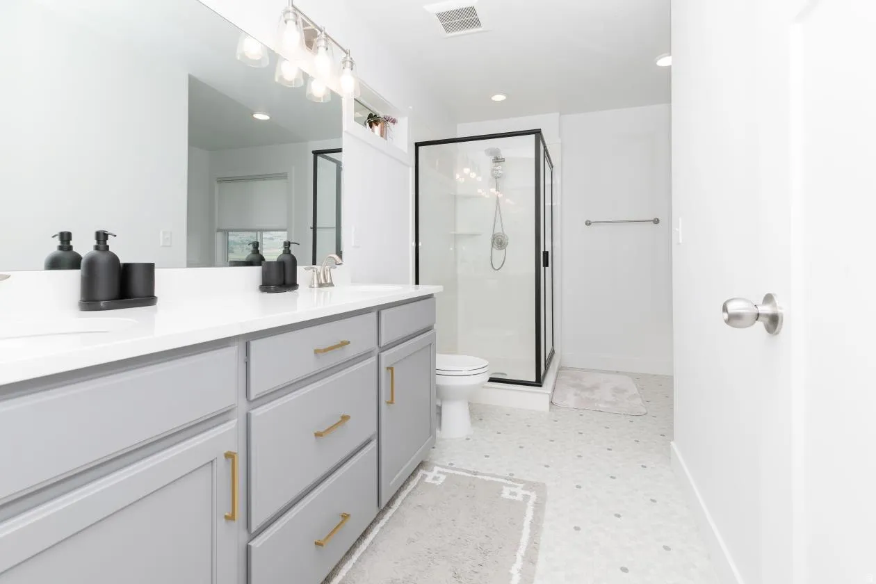 Dual sink vanity with light gray cabinetry and gold-tone hardware